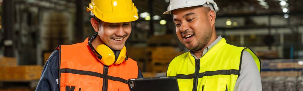 Imagem de 2 trabalhadores usando EPIs com um tablet nas mãos.