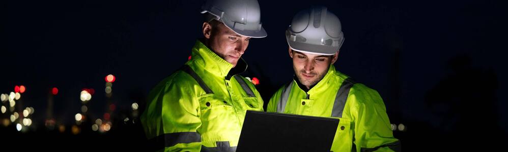 Trabalhadores usando EPIs utilizando dispositivo móvel à noite.